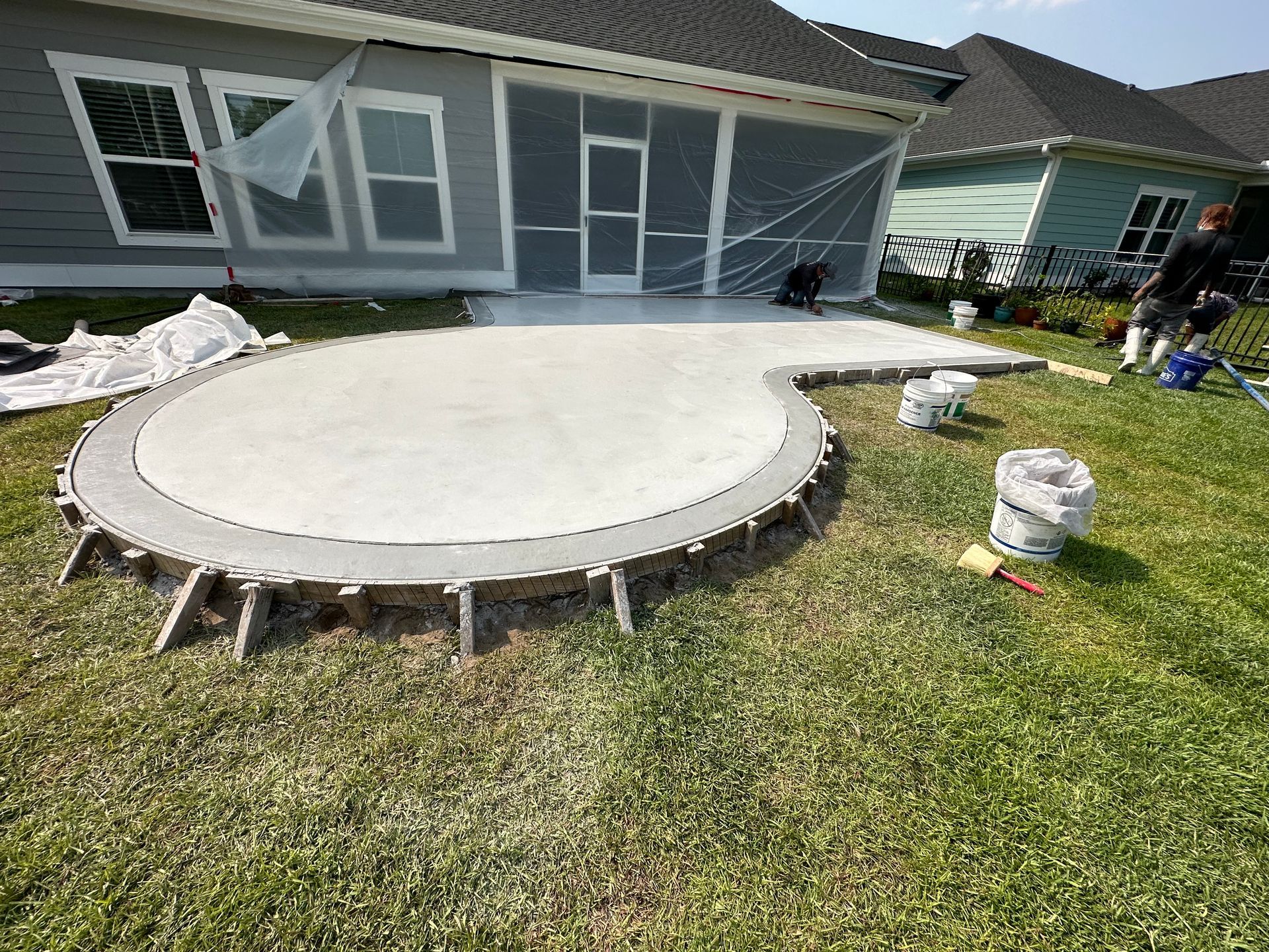 Backyard with a circular concrete patio under construction beside a screened porch; tools and materials scattered nearby