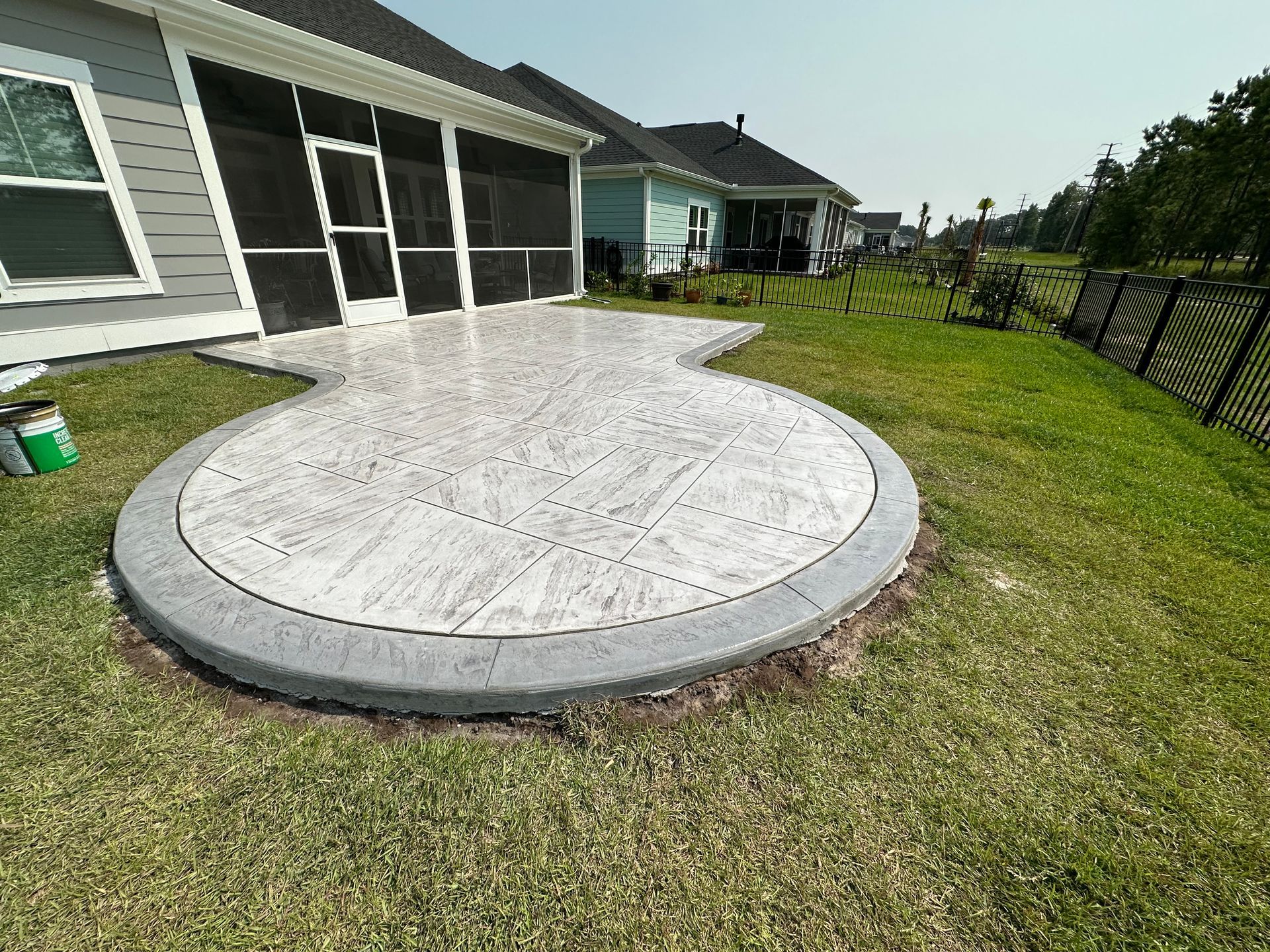 Patio with a circular concrete platform beside a house and fenced grassy yard