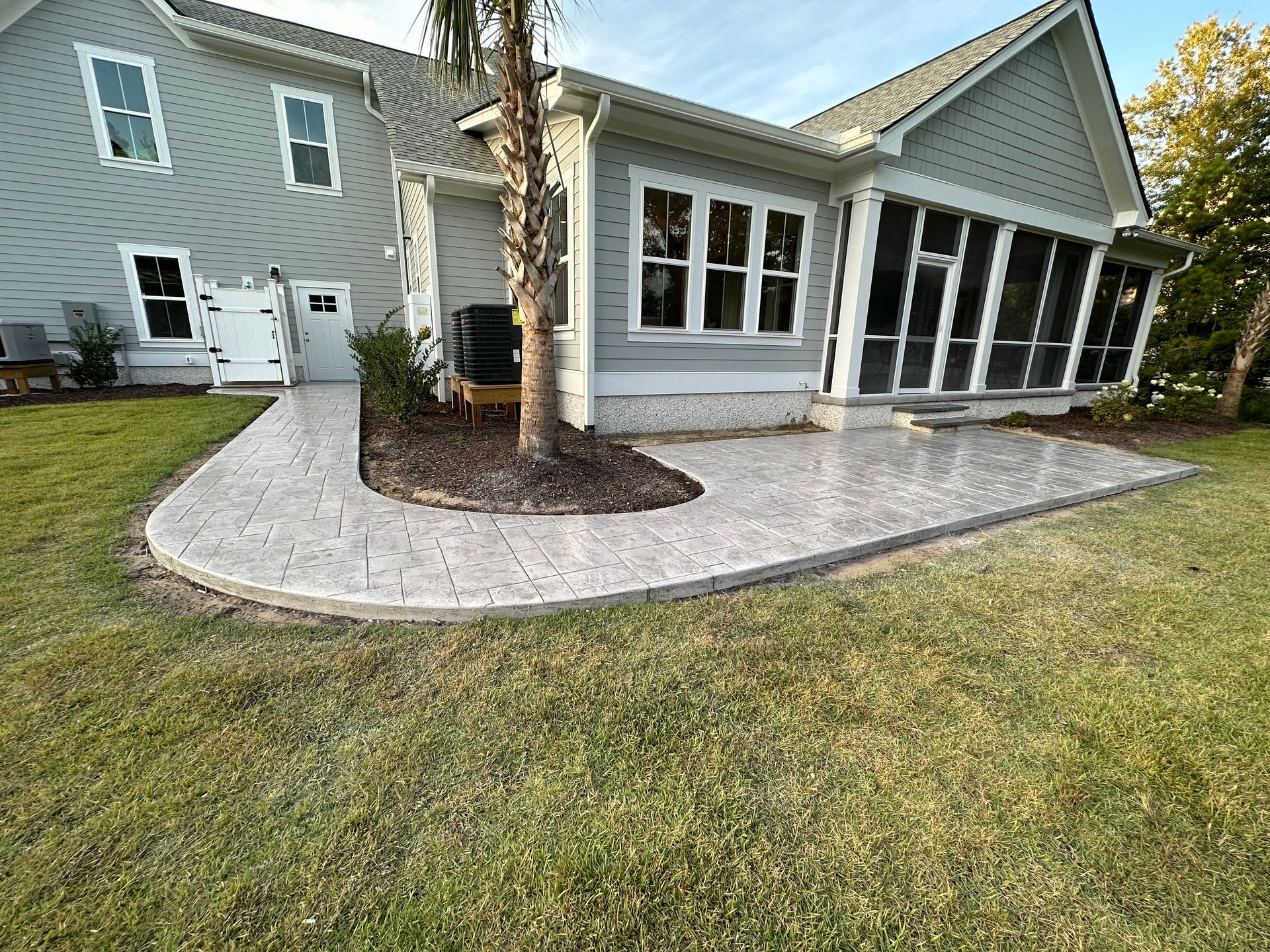 Curved paver walkway around palm tree leading to a gray house with a screened porch.