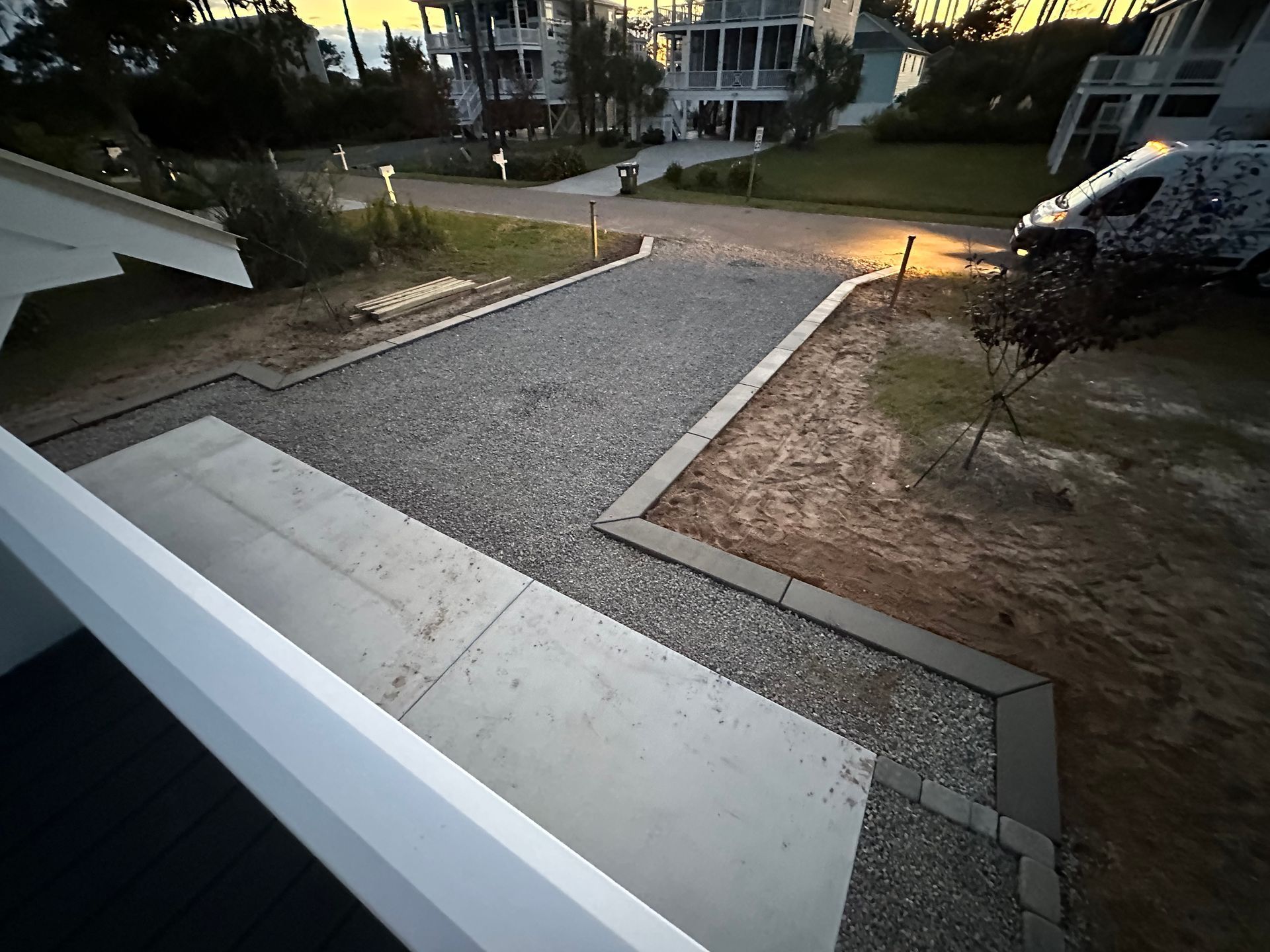 Front porch steps leading to a gravel driveway and road at dusk, with neighboring houses visible.