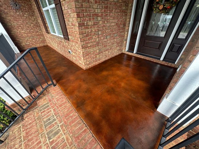Brick porch with dark-stained concrete floor and black railings by a front door
