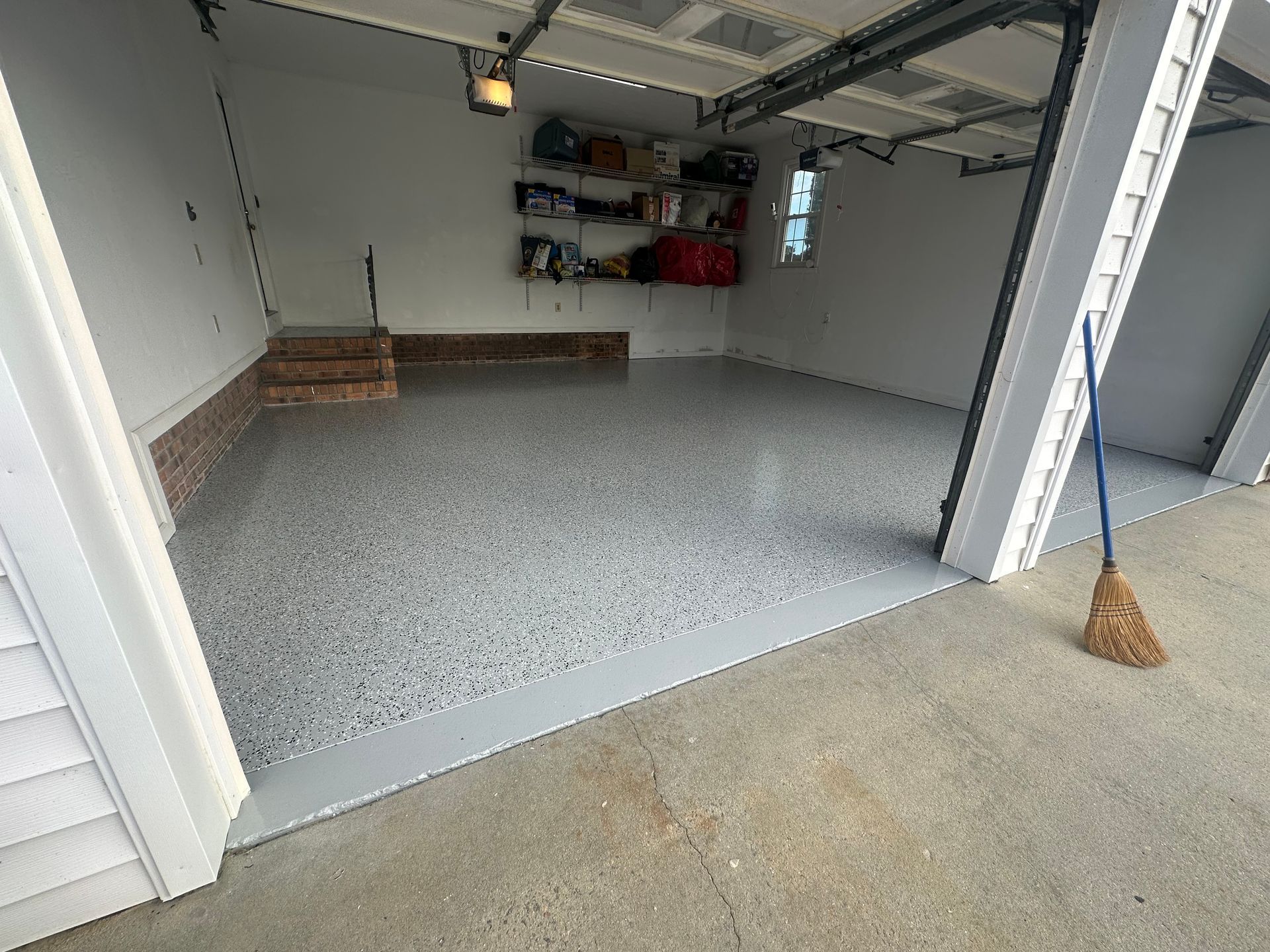 Empty garage with gray speckled floor, open door, and shelves on the back wall