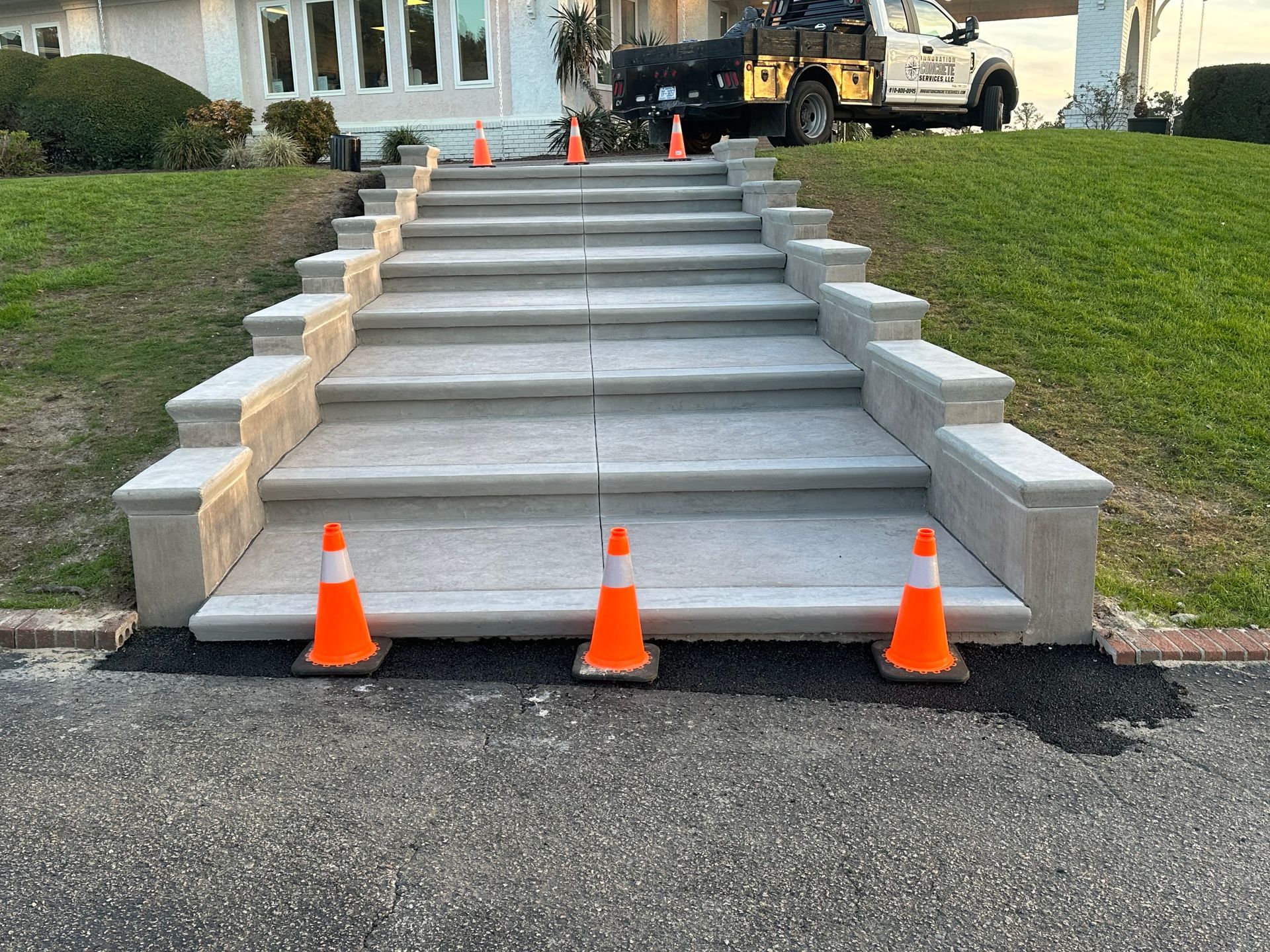 Outdoor steps under construction with concrete stair treads, orange cones, and a parked truck nearby