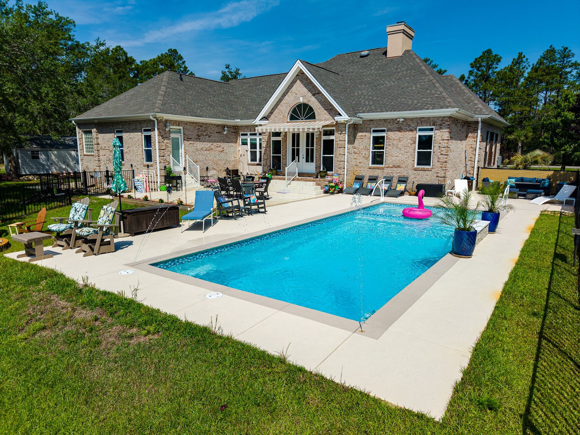 Stone house with a backyard pool, lounge chairs, and patio seating on a sunny day