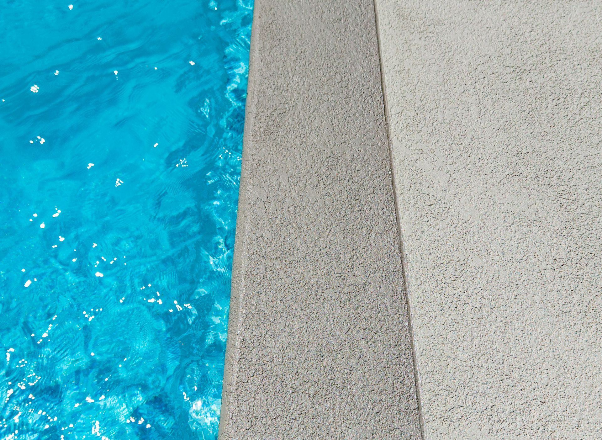 Blue pool water beside a textured gray concrete edge and white deck.