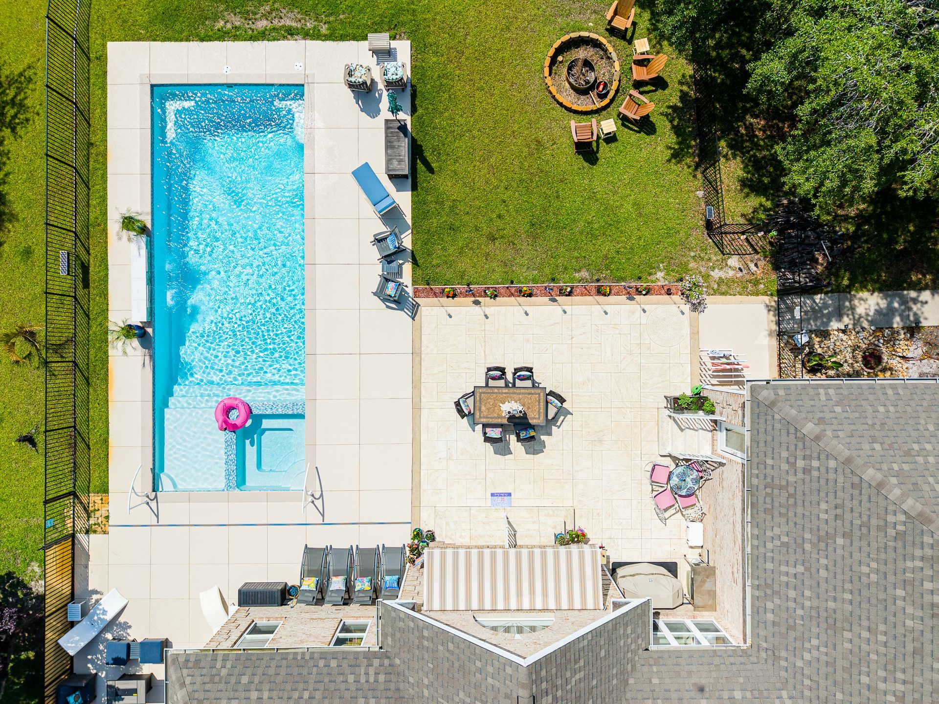 Aerial view of a backyard with a swimming pool, patio furniture, and a grassy area with a fire pit.