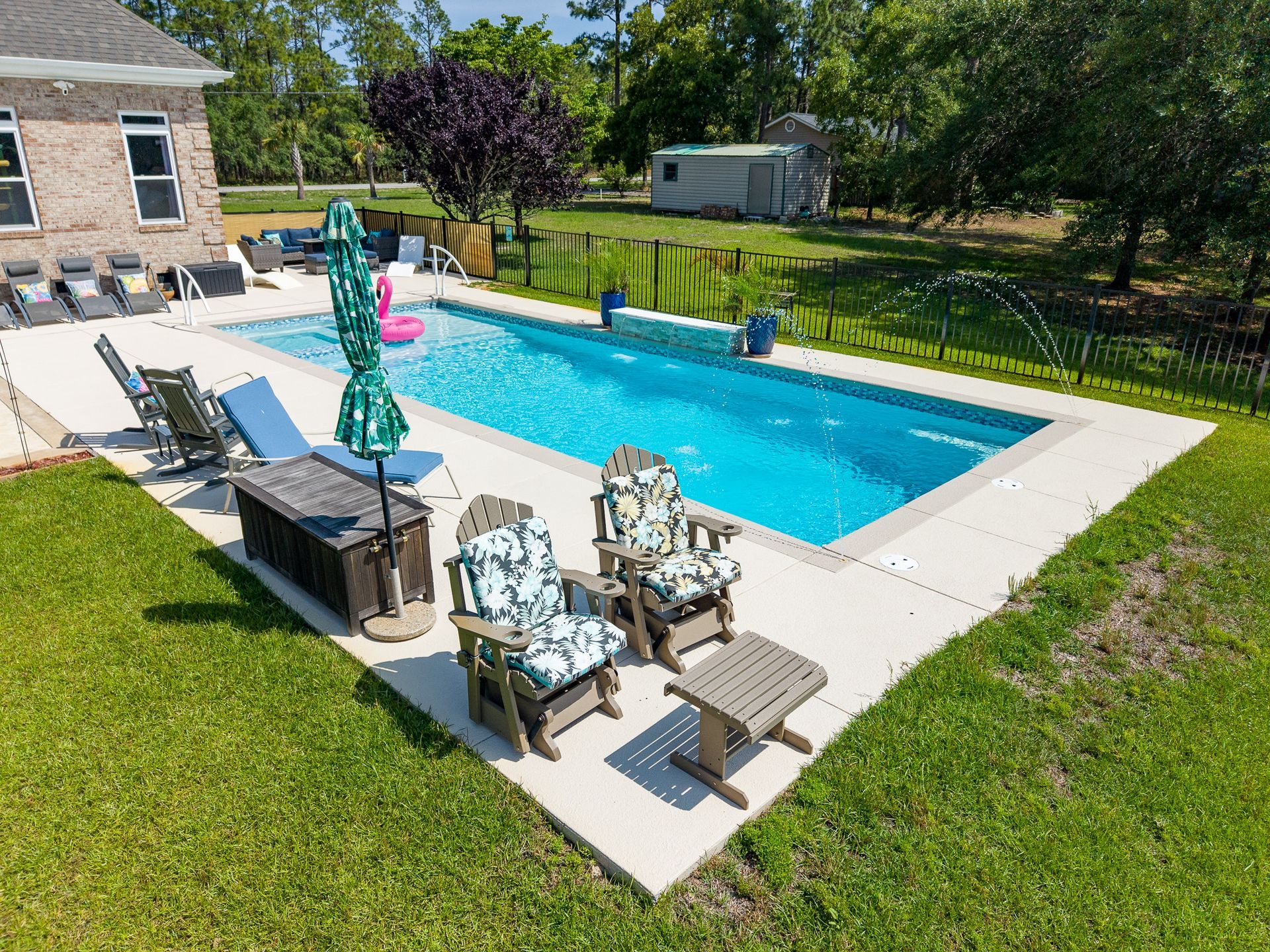 Backyard pool with turquoise water, patio chairs, and an umbrella beside a house and lawn