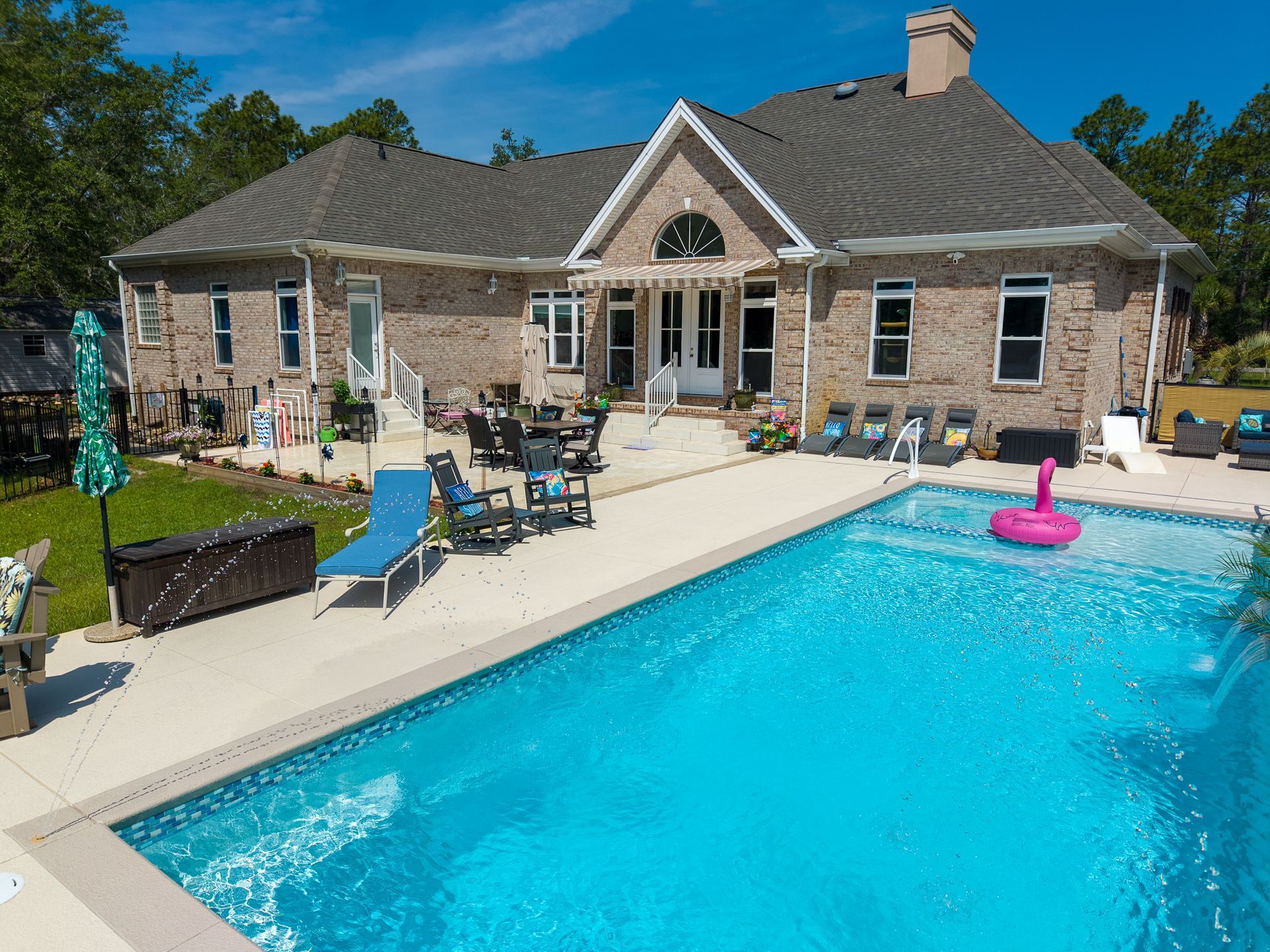 Backyard pool beside a stone house with lounge chairs and a pink floatie under a blue sky