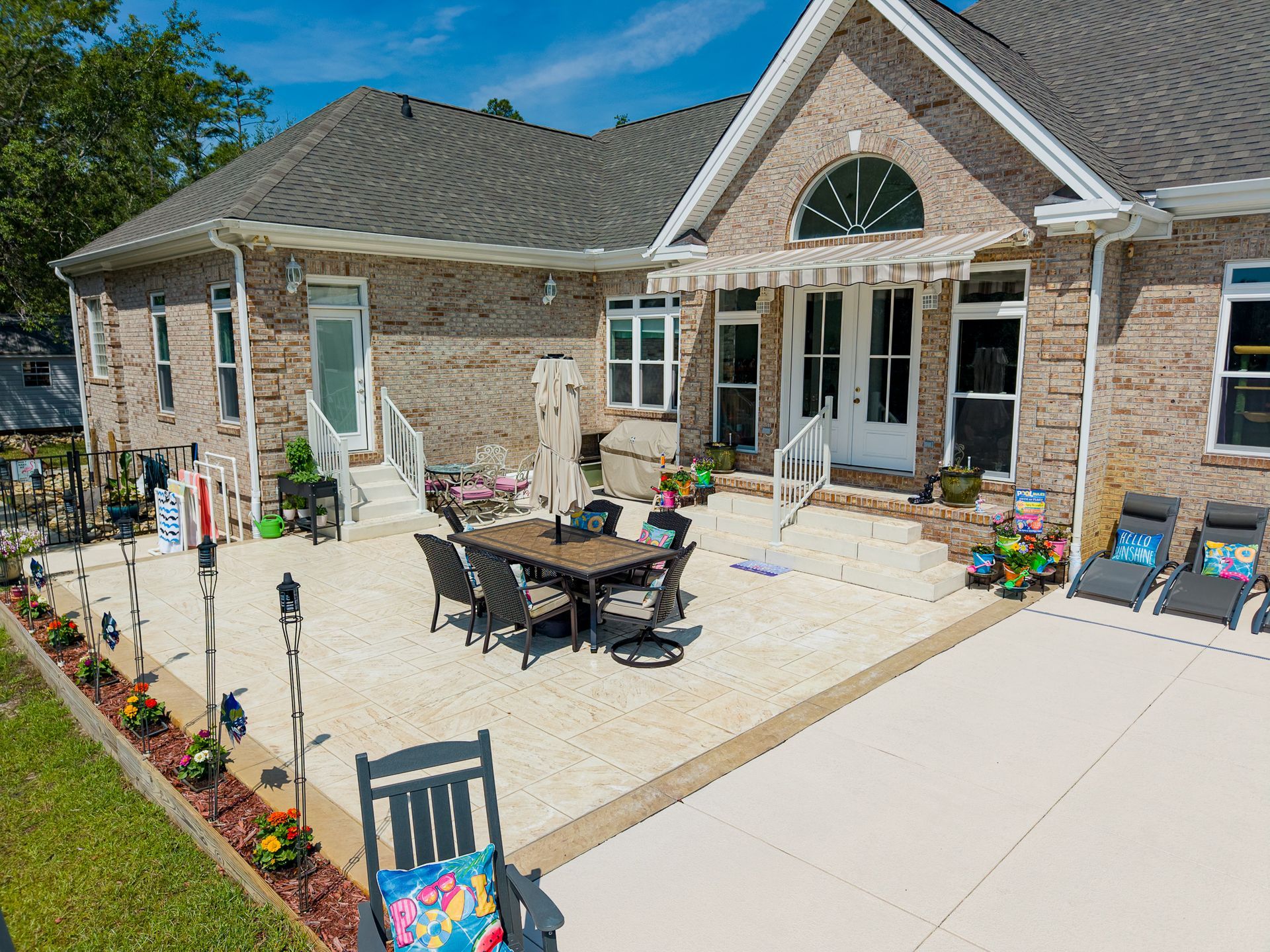 Stone patio with outdoor dining table and chairs beside a brick house under a blue sky