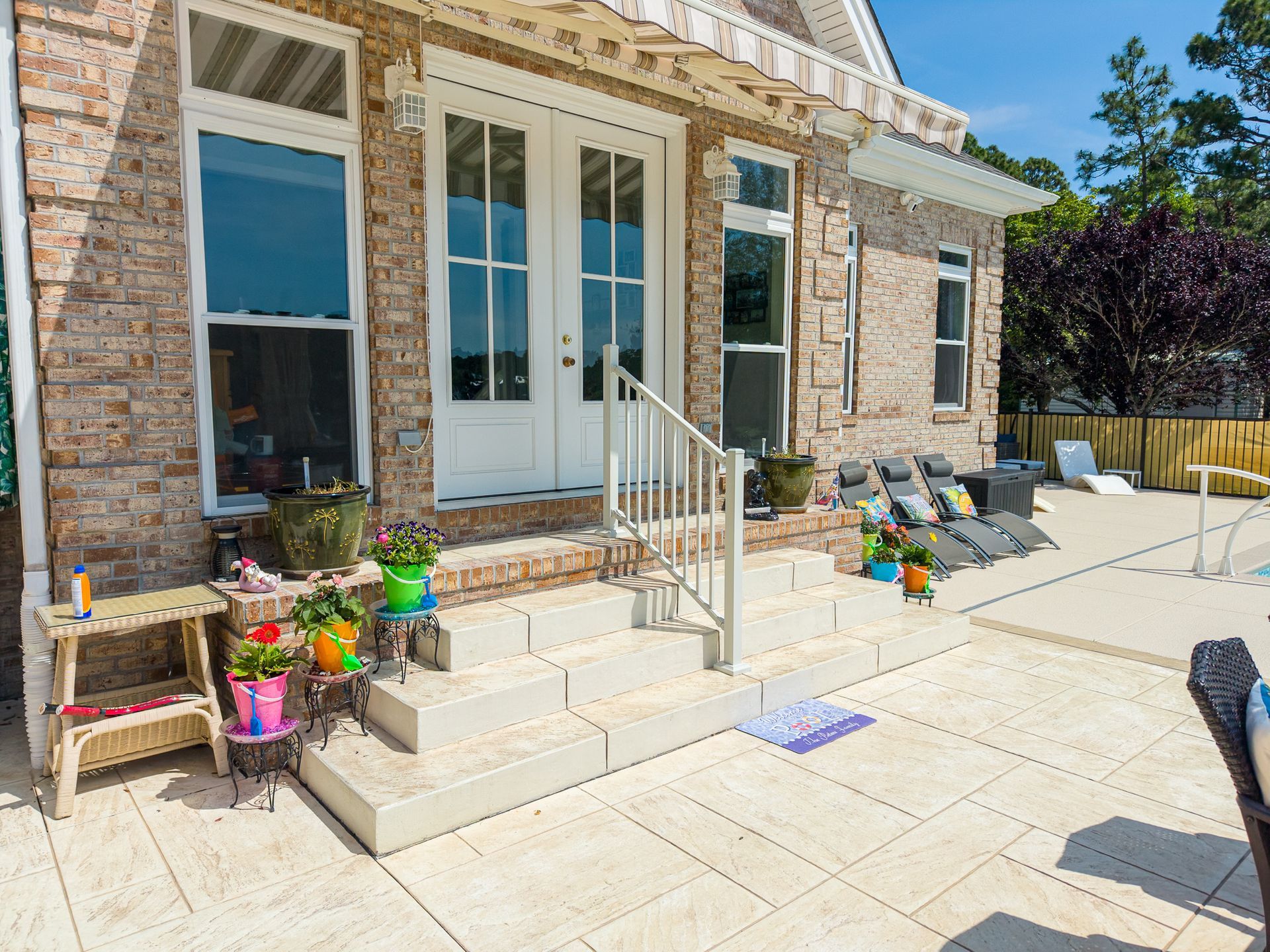 Brick house patio with white French doors, steps, potted plants, and sunlit stone paving