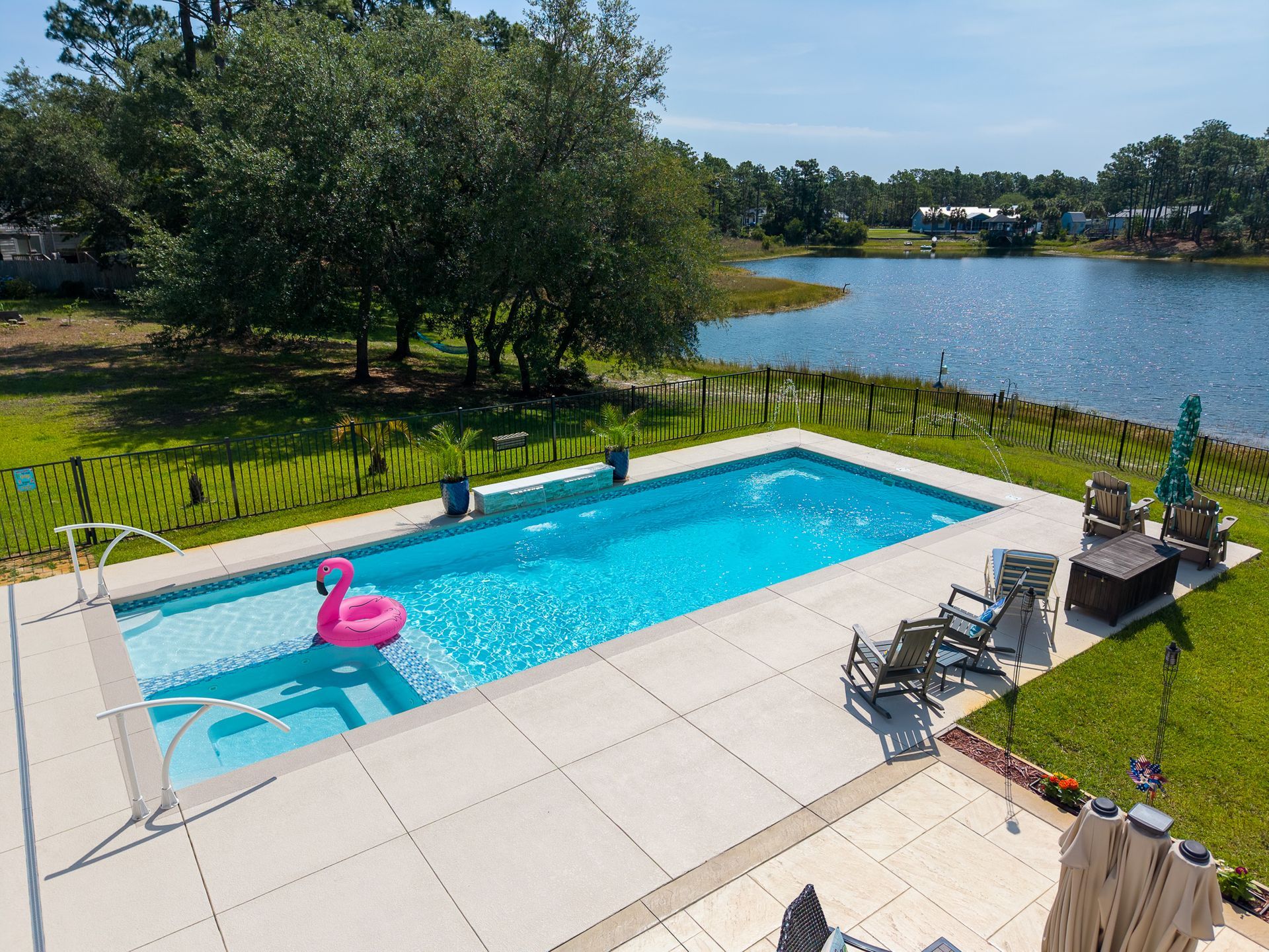 Backyard pool with pink flamingo float, lounge chairs, and lake view on a sunny day