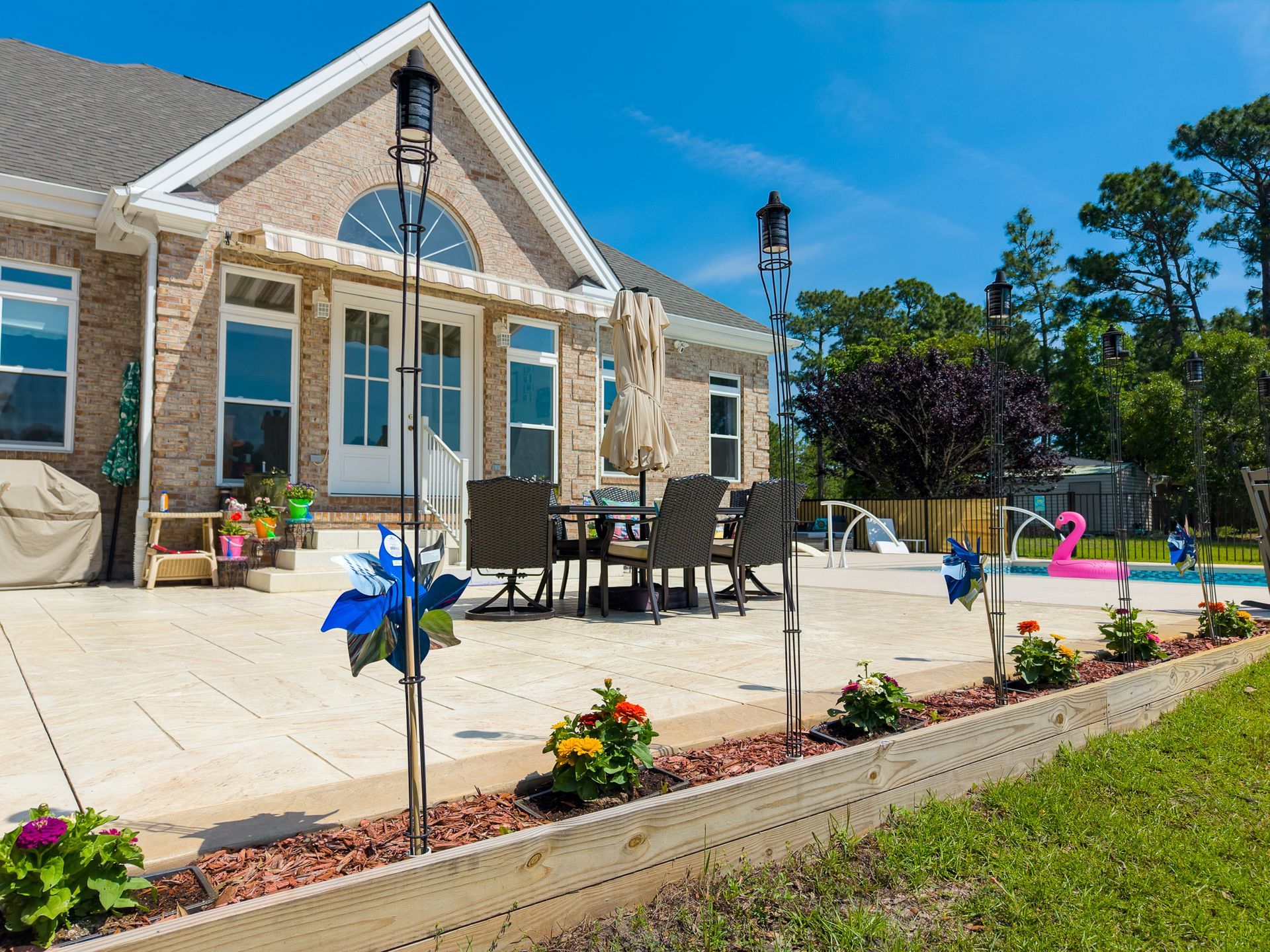 Backyard patio with outdoor dining set, umbrella, and colorful flowers beside a brick house