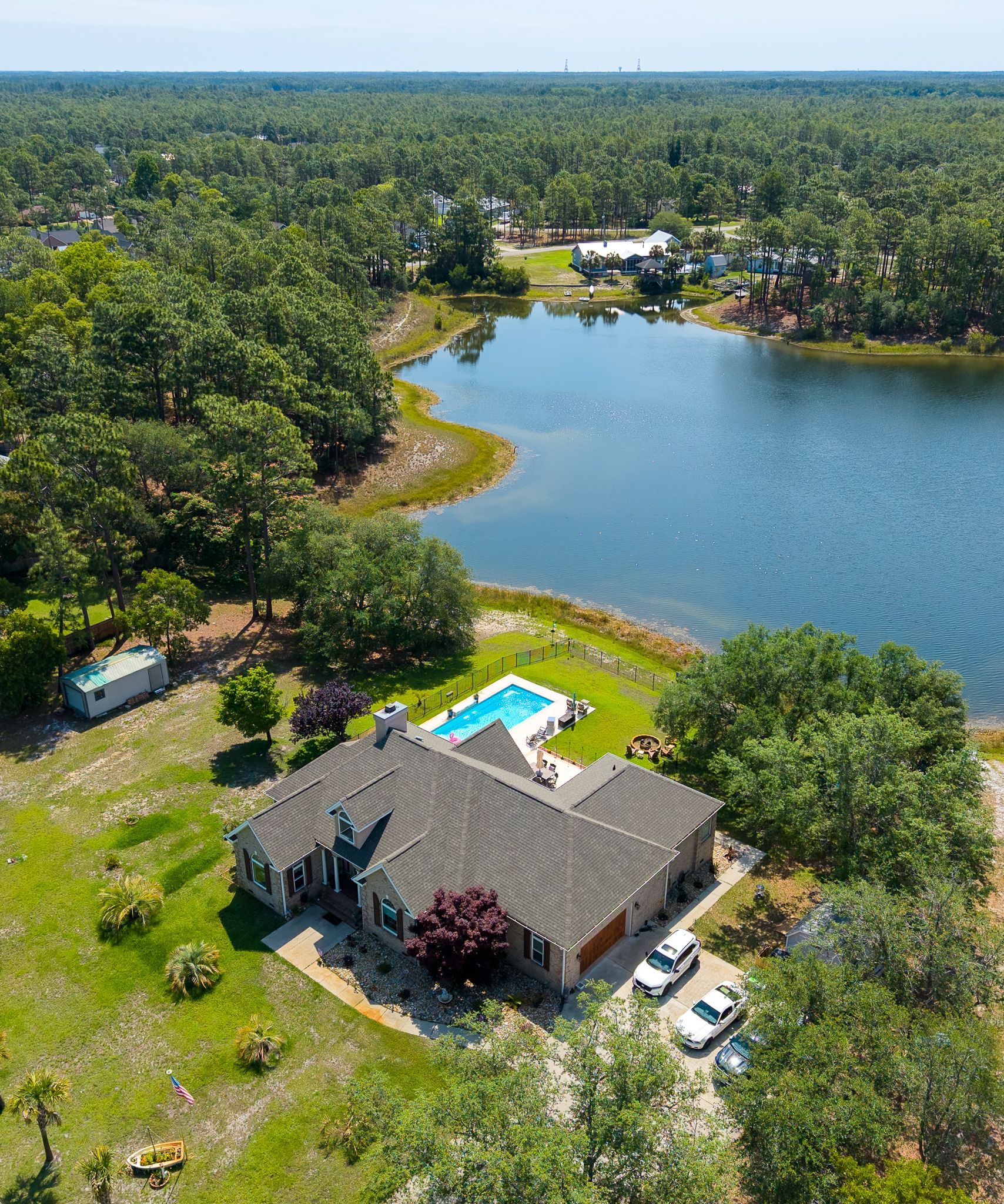 Aerial view of a lakeside house with a swimming pool surrounded by trees and water