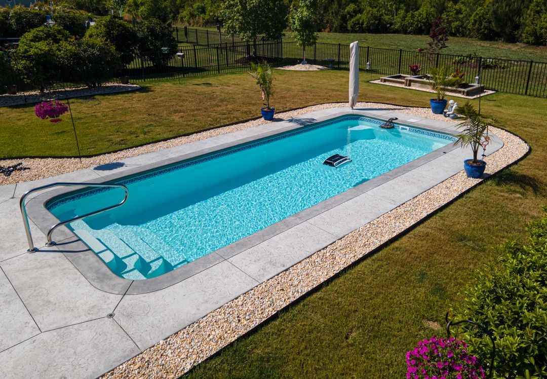 Rectangular backyard swimming pool with clear blue water, white coping, and a grassy garden around it