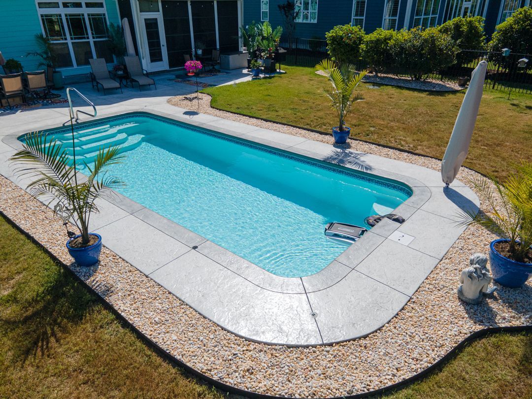 Outdoor swimming pool with blue water, stone deck, and lawn in a sunny courtyard