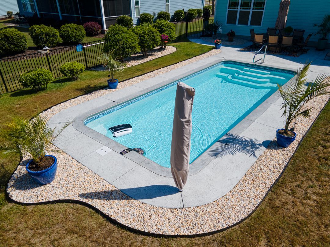 Backyard swimming pool with a lounge chair, blue pots, and a covered post on a sunny day