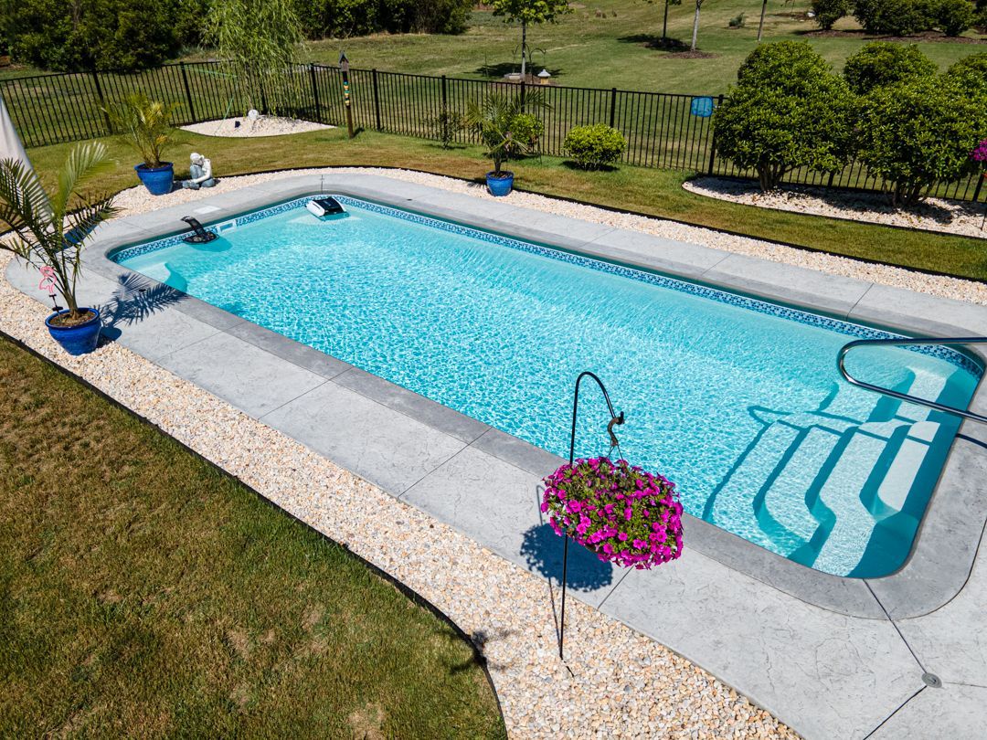 Backyard swimming pool with clear blue water, white stone deck, and flower planters on the side
