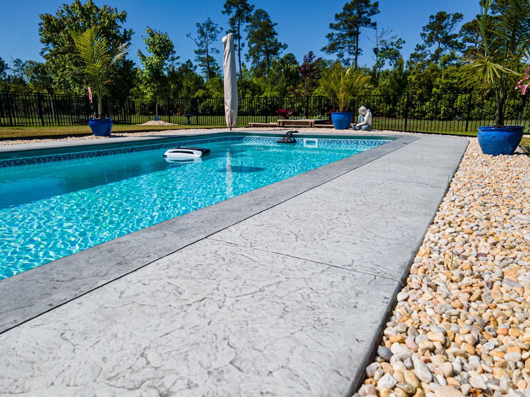 Backyard swimming pool with turquoise water, concrete deck, and trees under a clear blue sky