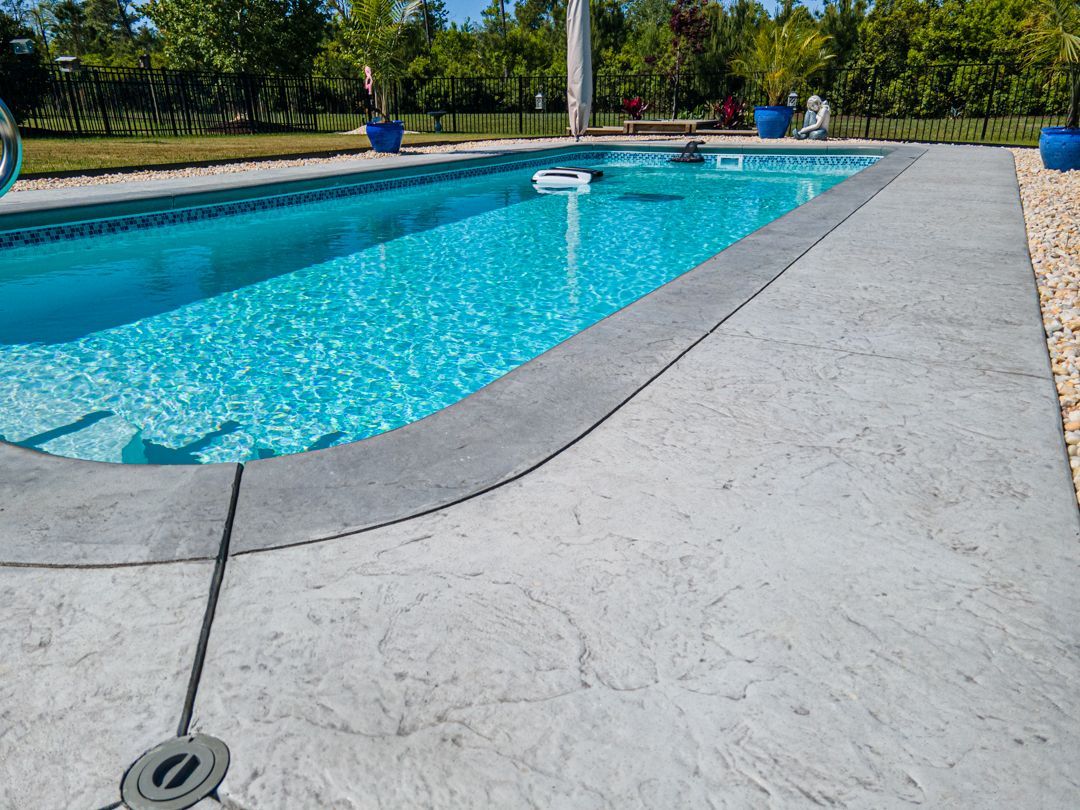 Outdoor swimming pool with clear blue water, gray deck, and green trees in the background
