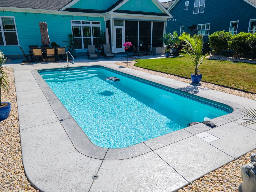 Backyard swimming pool beside a turquoise house, with patio paving and lawn