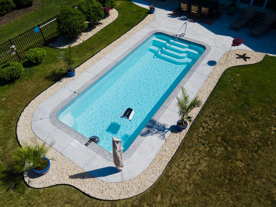 A rectangular outdoor swimming pool with blue water, white paving, and green lawn around it.