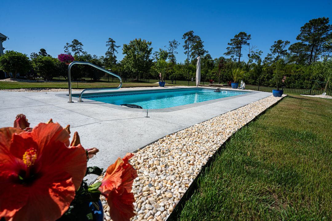 Outdoor swimming pool with a water slide, white gravel border, and red flowers in the foreground