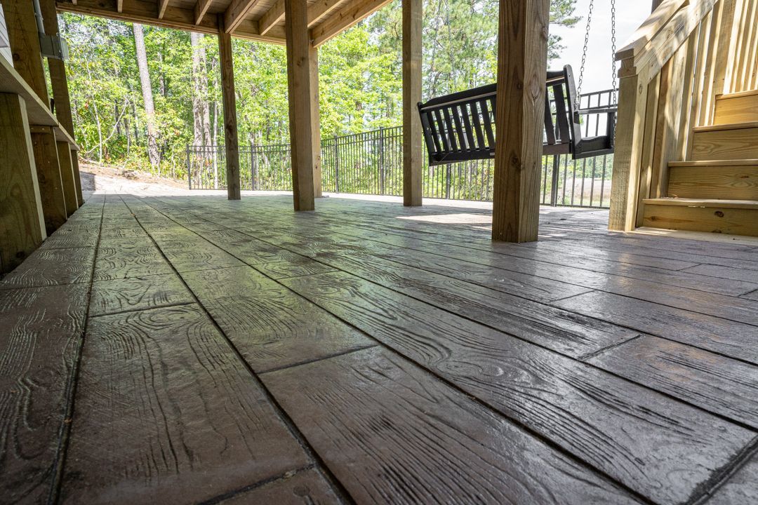 Covered wooden porch with weathered floorboards and a staircase, overlooking a wooded area