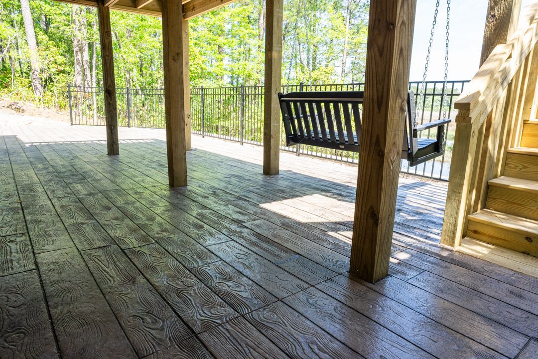 Wooden porch with railings and a hanging swing overlooking a wooded yard