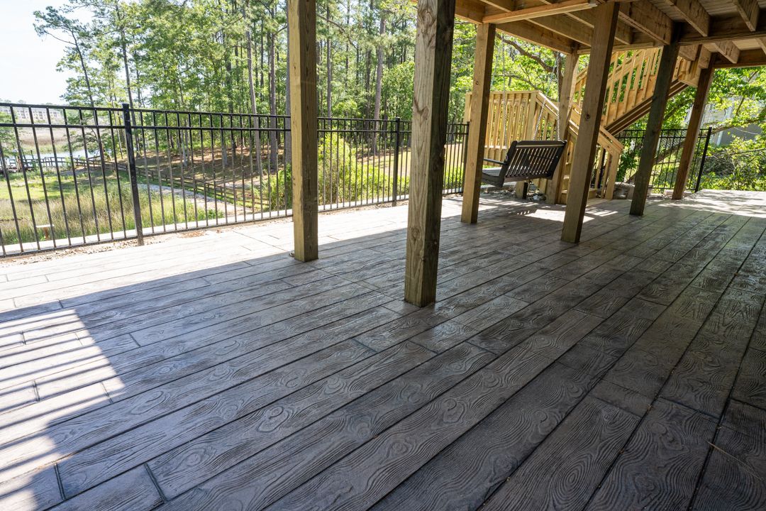 Covered wooden deck with black railing and sunlit yard view outside