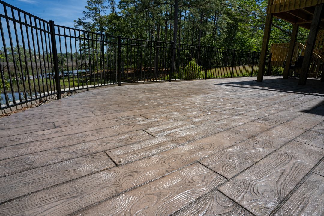 Stone patio with black metal railing, overlooking trees and distant hills under a bright blue sky