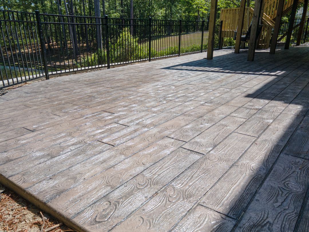 Empty concrete patio beside a black metal fence, partly shaded by trees.