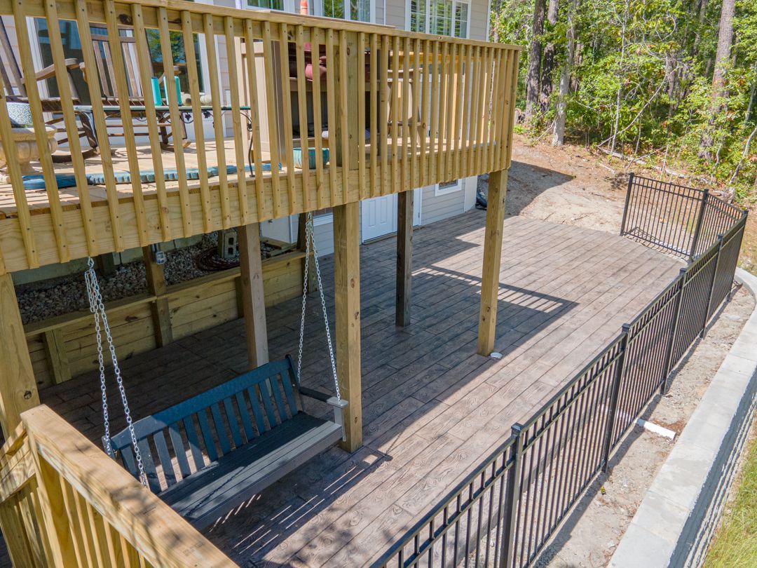 Backyard deck with wooden stairs, railing, and a swing beneath, beside a black metal fence