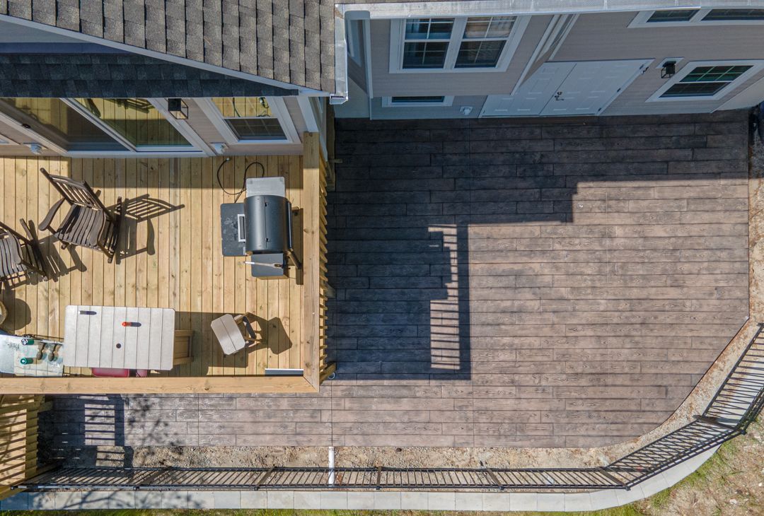 Aerial view of a wooden deck with patio furniture beside a fenced backyard and house exterior.