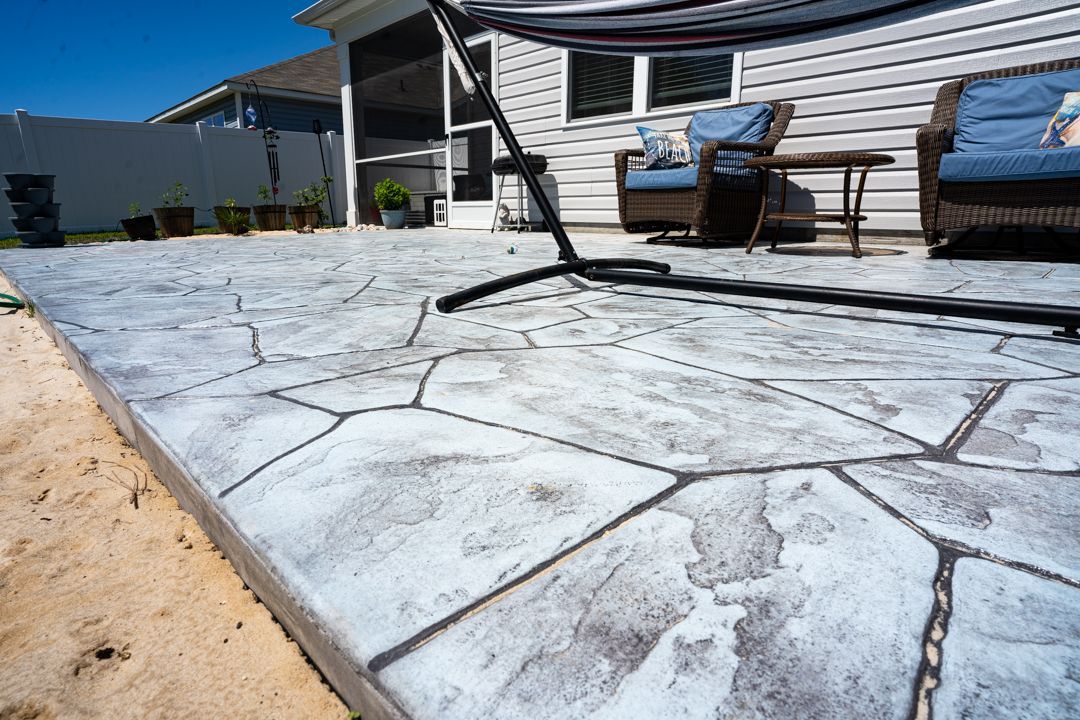 Stamped concrete patio beside a house, with outdoor chairs and a sandy yard
