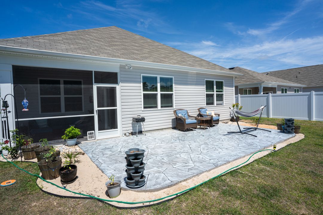 Backyard patio with pavers, outdoor seating, potted plants, and a screened porch beside a white house