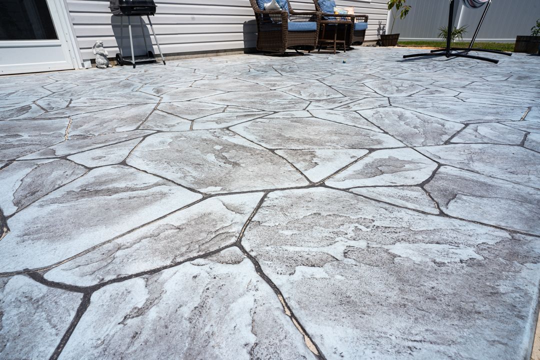 Stamped concrete patio with a cracked stone pattern, outdoor seating in the background.