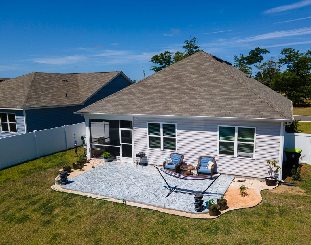 Backyard patio with two blue chairs, white gravel, and a white house with gray roof