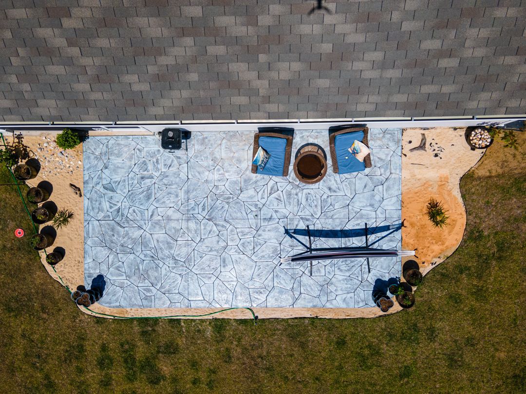 Overhead view of a backyard patio with a blue tarp, chairs, a fire pit, and surrounding lawn