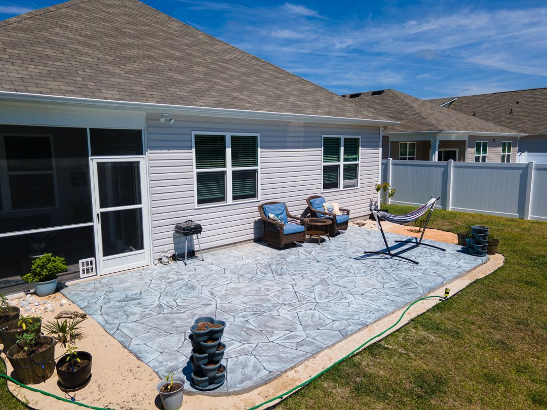 Backyard patio with lounge chairs, small table, and blue-gray gravel beside a house under a bright sky