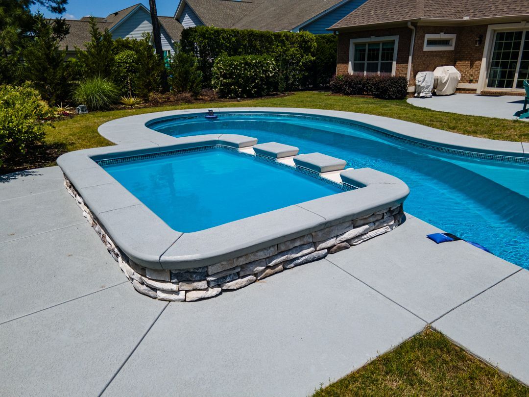 Backyard pool with attached spa, blue water, and white stone deck under a sunny sky