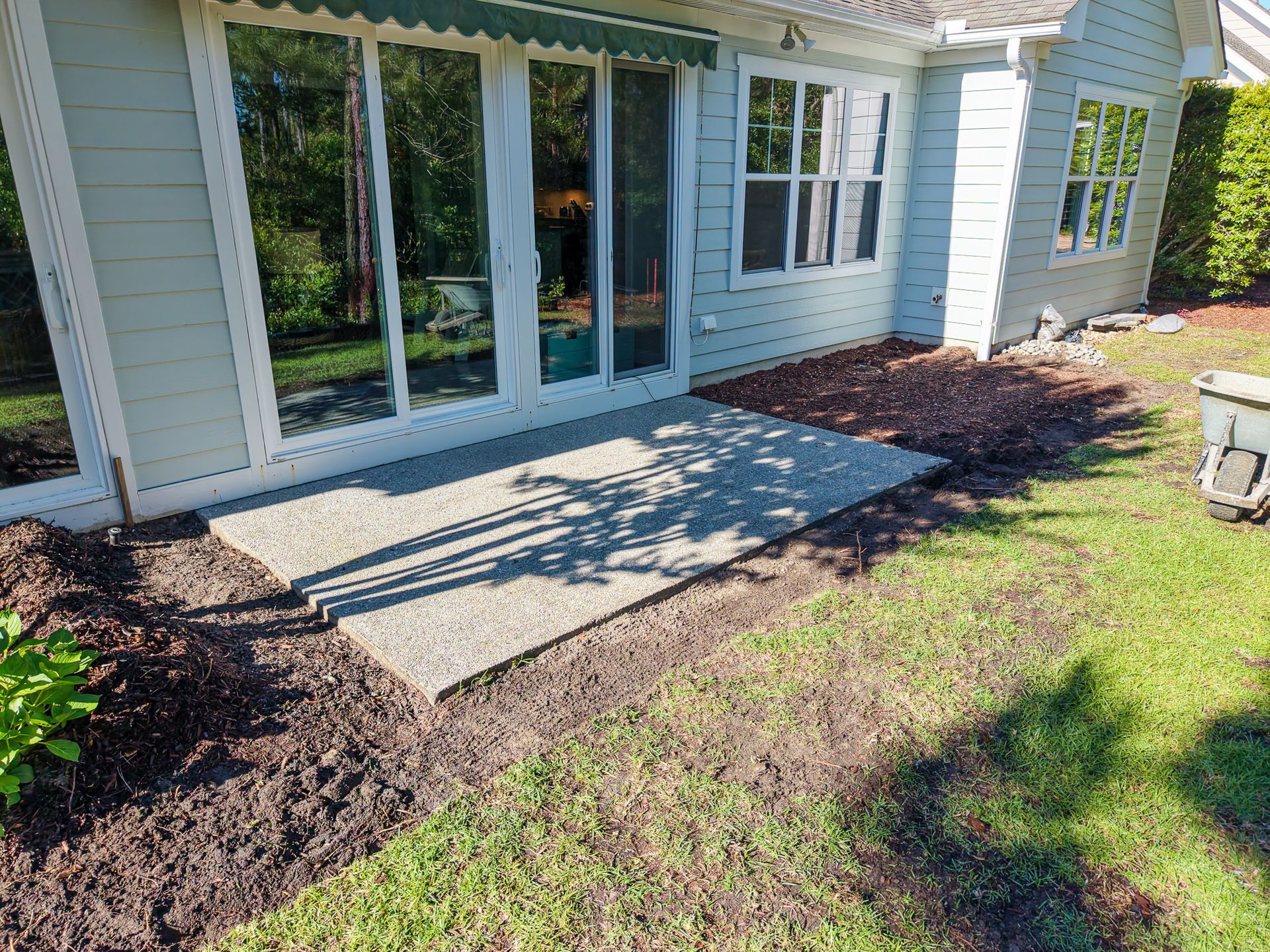 Patio area with sliding glass doors, concrete slab, mulch beds, and lawn beside a house