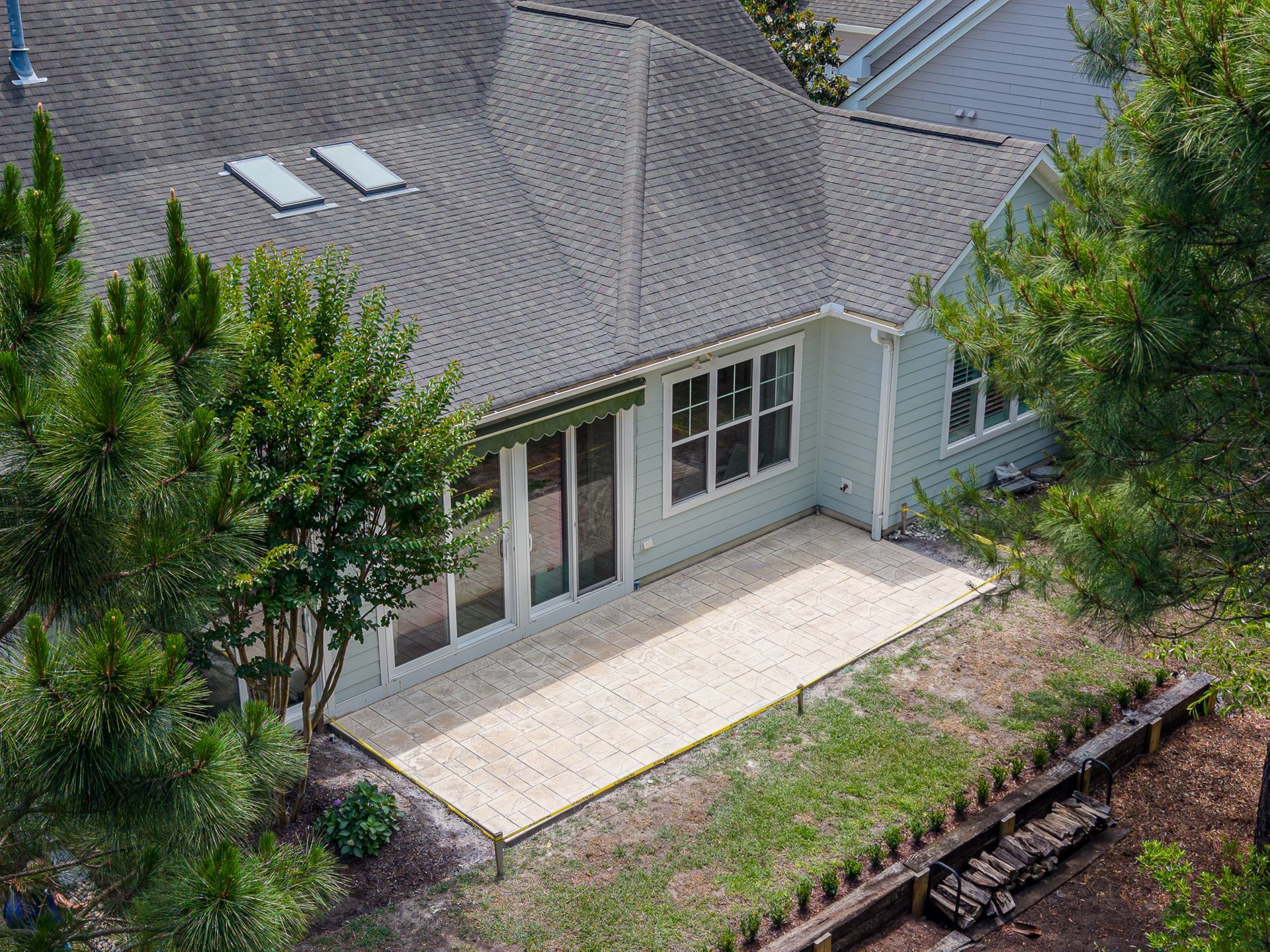 Aerial view of a house roof, patio, and surrounding trees beside a narrow waterway.