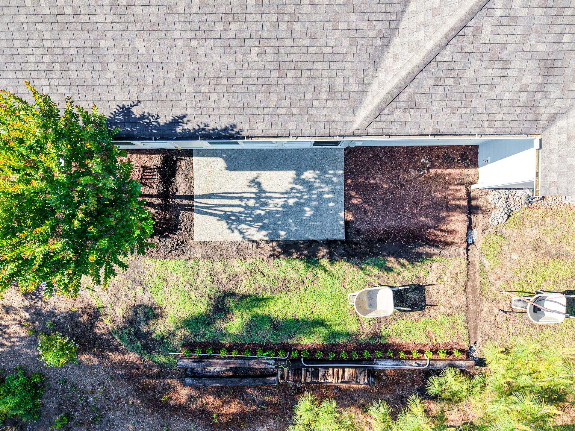 Top-down view of a house roof edge, with trees, bushes, and a small driveway or walkway below.