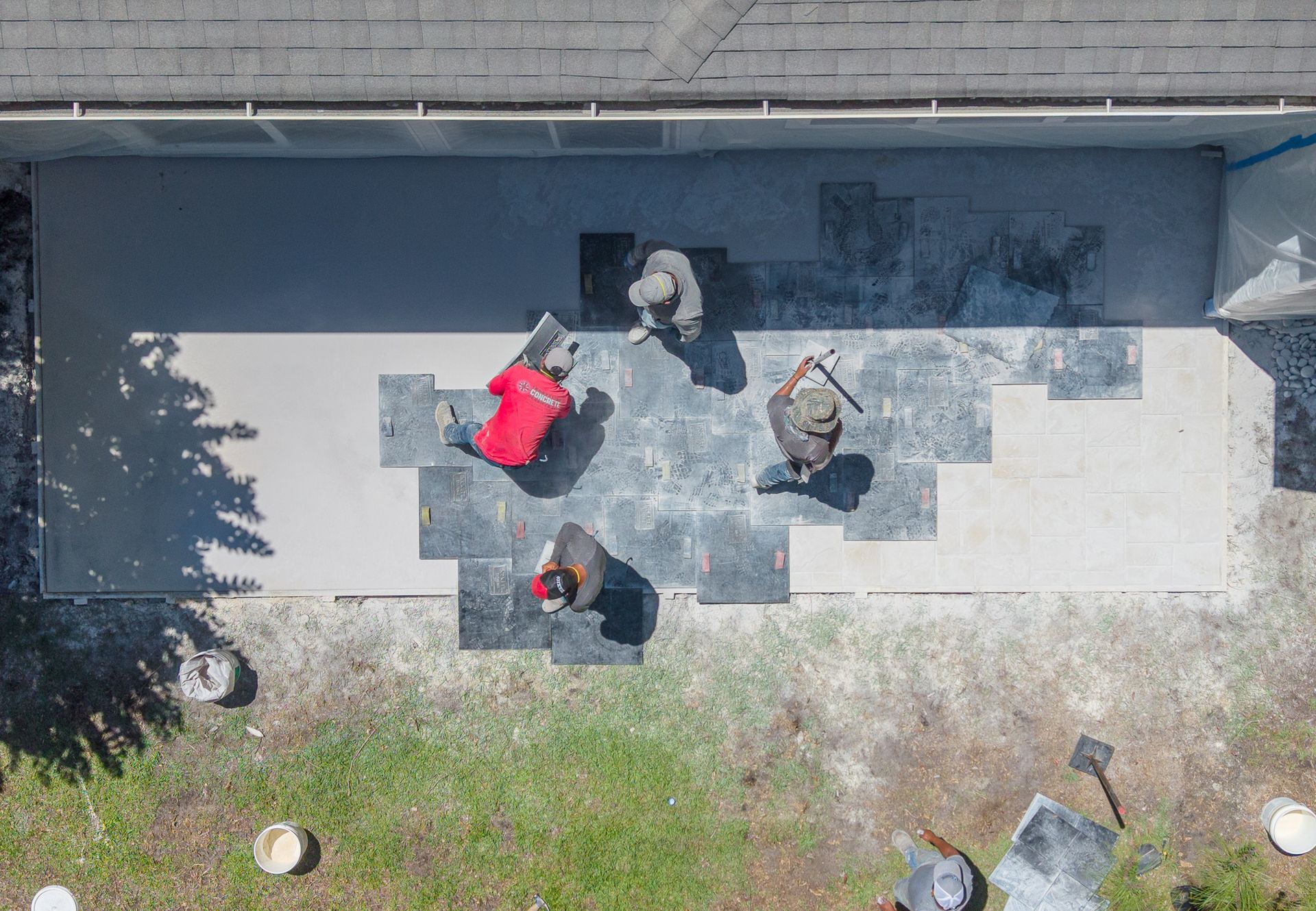 Aerial view of four people on a concrete walkway beside a wall and grass, one wearing a bright red jacket.