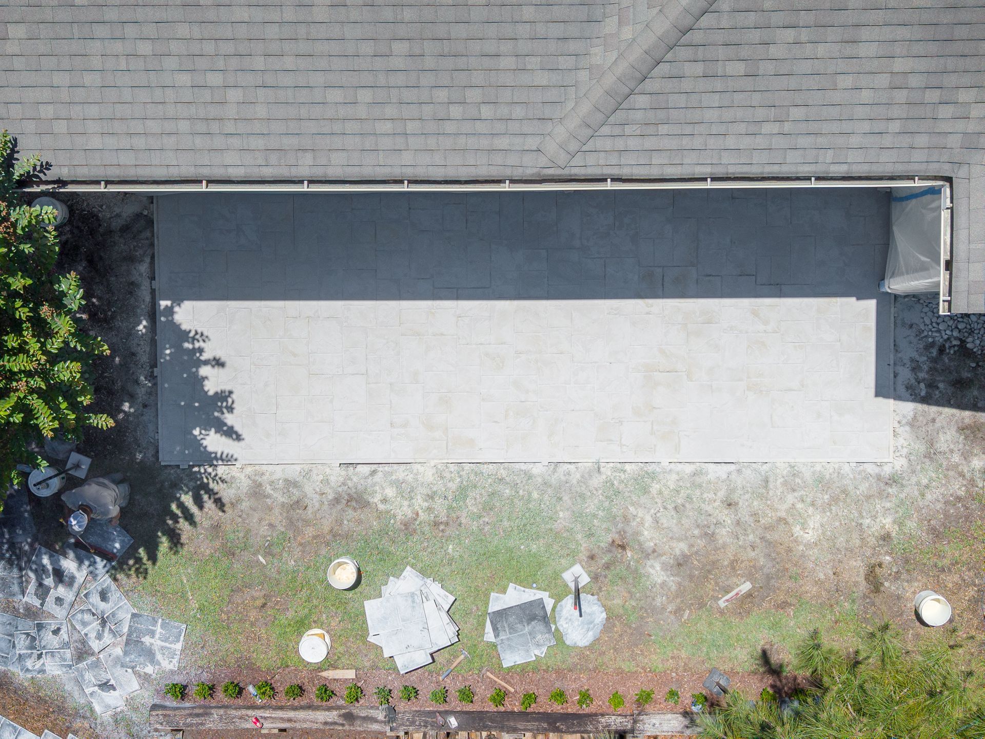 Aerial view of a rooftop with a large white patio area and a small garden strip along the edge.