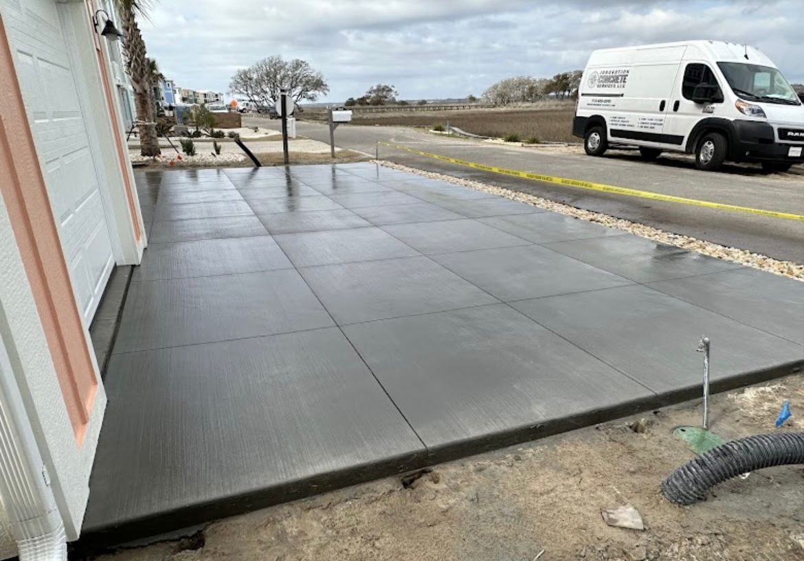 Freshly poured concrete sidewalk beside a building, with a white van parked on the street.