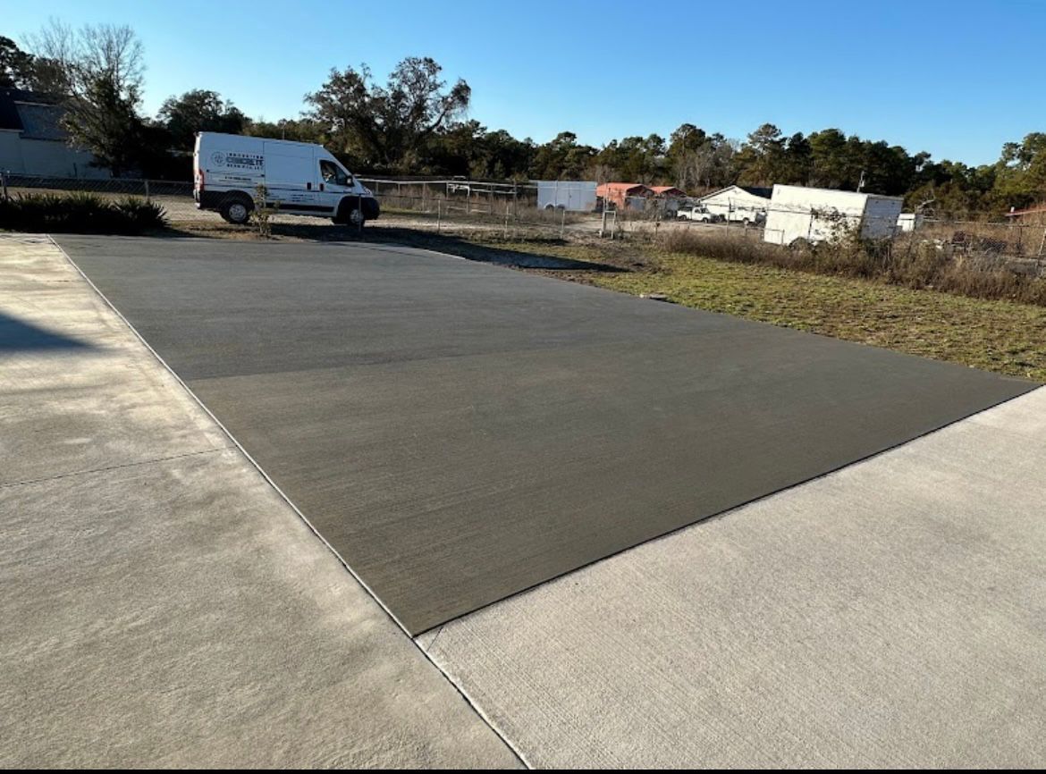 Freshly paved dark asphalt section beside a concrete driveway, with a white van in the background.