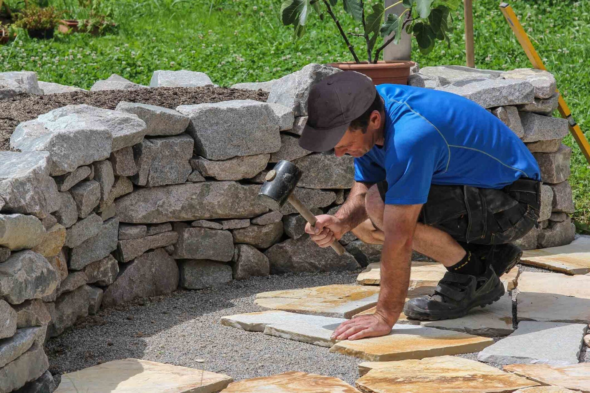 Worker laying stone pavers beside a stacked stone wall outdoors