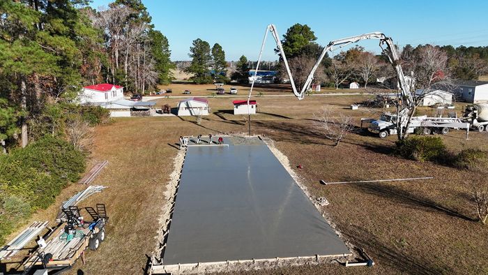 Concrete foundation slab on a cleared lot with construction equipment and trees in the background