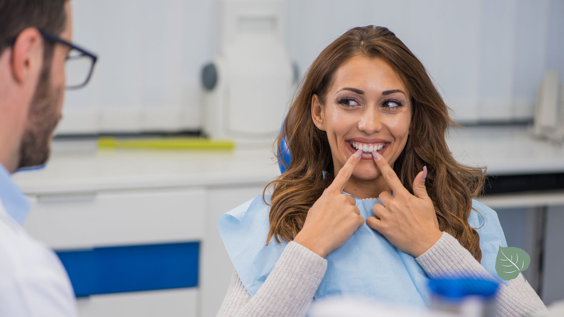 A woman is sitting in a dental chair looking at her teeth.